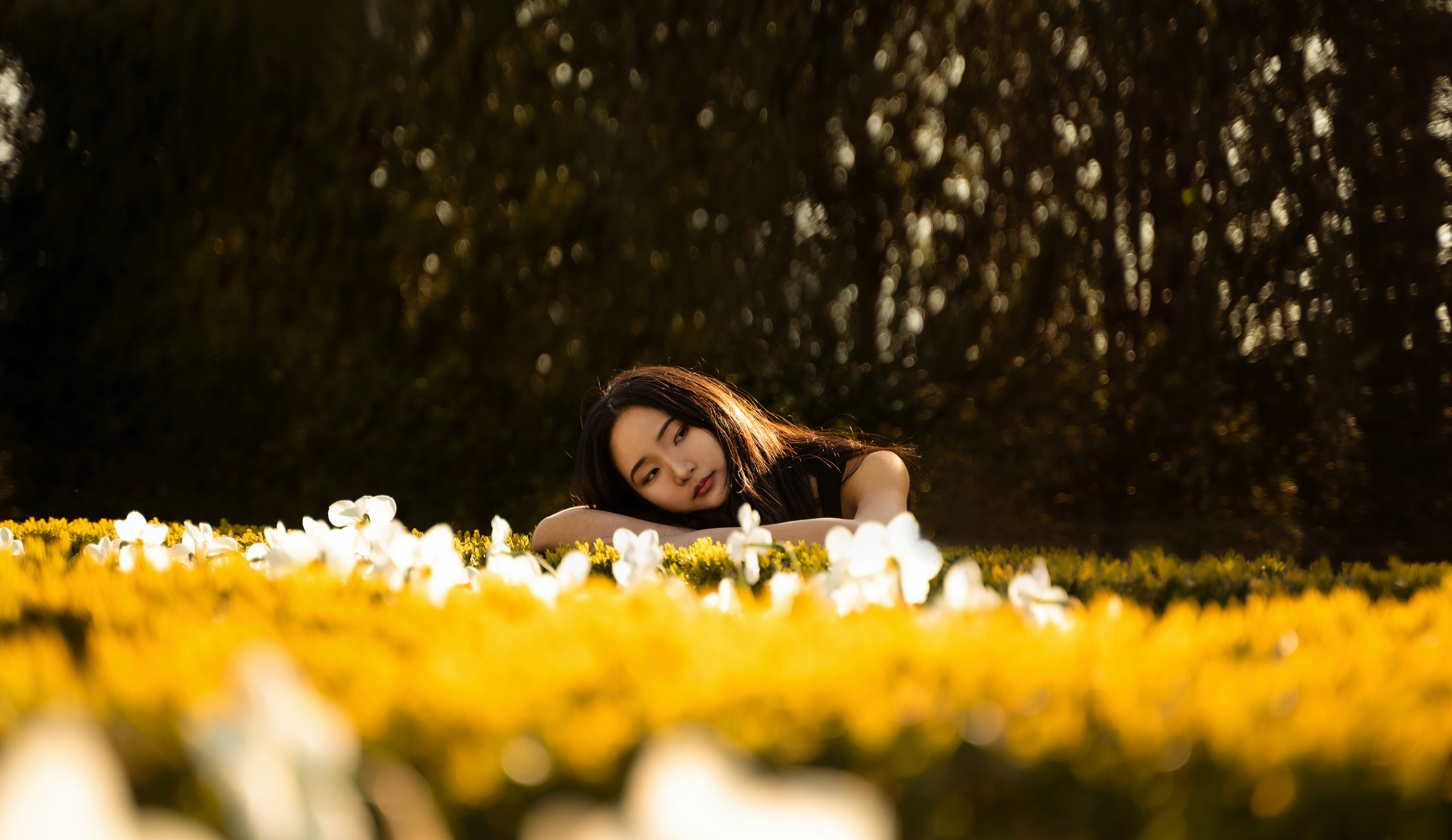 woman in white tank top lying on yellow flower field during daytime